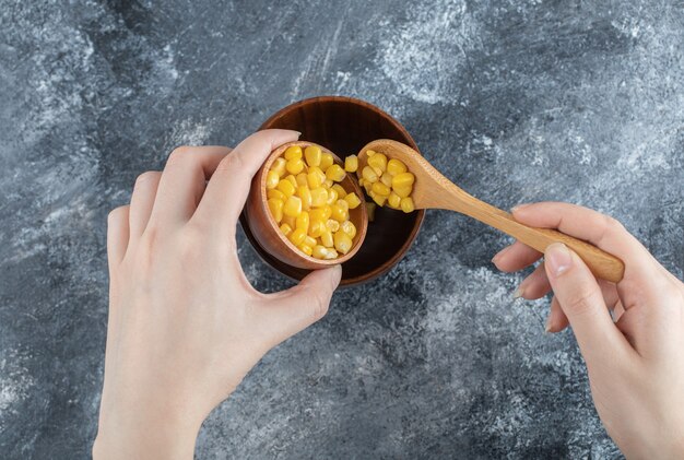 Hand adding popcorn seeds into a wooden bowl.
