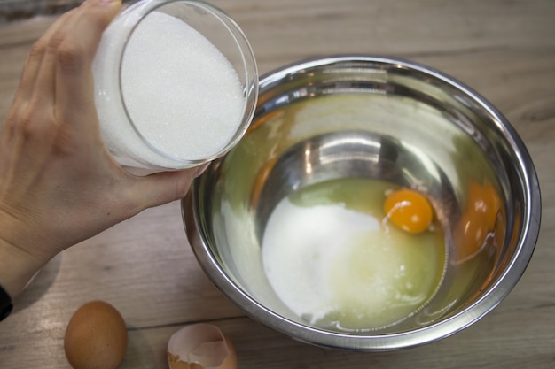 계란이 있는 금속 그릇에 손으로 설탕을 추가합니다.