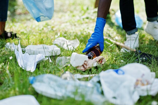 Hand of african american man picking up bottle into garbage bags while cleaning area in park Africa volunteering charity people and ecology concept