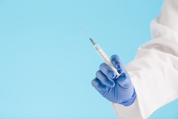 Hand in a blue glove holding syringe on blue