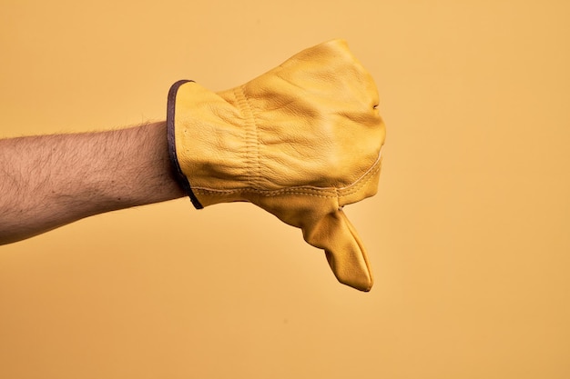 Foto gratuita mano del giovane caucasico con guanto da giardiniere su sfondo giallo isolato facendo il pollice verso il basso gesto di rifiuto disapprovazione antipatia e segno negativo