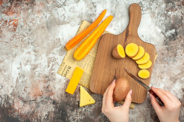 Hand chopping various vegetables and two kinds of cheese knife on wooden cutting board on an old newspaper on mixed color background