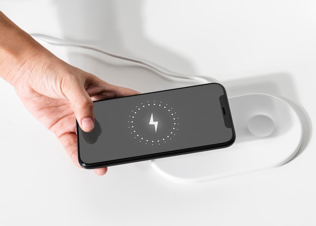 Бесплатное фото Рука, подключающая смартфон к беспроводному зарядному устройству