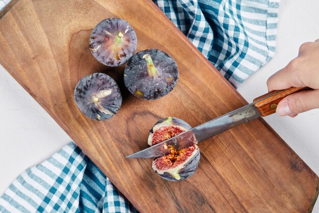 Hand cutting a fig on wooden cutting board with a blue tablecloth.