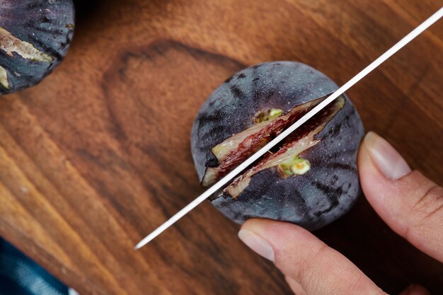 Hand cutting a fig on wooden cutting board.