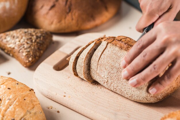 Hand cutting loaf of bread with knife on chopping board