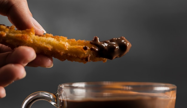 Hand dipping a fried churros in chocolate close-up