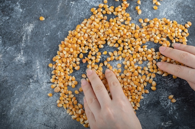 Hand distributing uncooked popcorn seeds on marble.