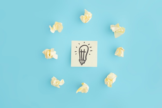 Free photo hand drawn light bulb on sticky note surrounded with crumpled paper on blue backdrop