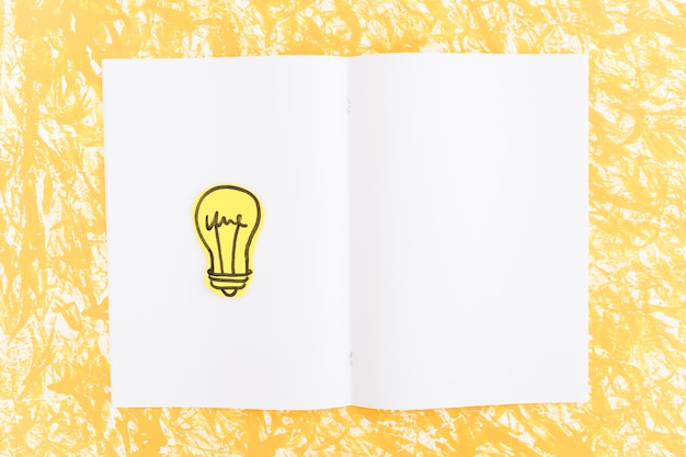 Hand drawn light bulb on white page over the yellow textured backdrop
