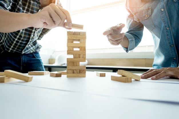 Foto gratuita mano di ingegnere che gioca un gioco di torre di legno di un blocco (jenga) sul disegno o progetto architettonico