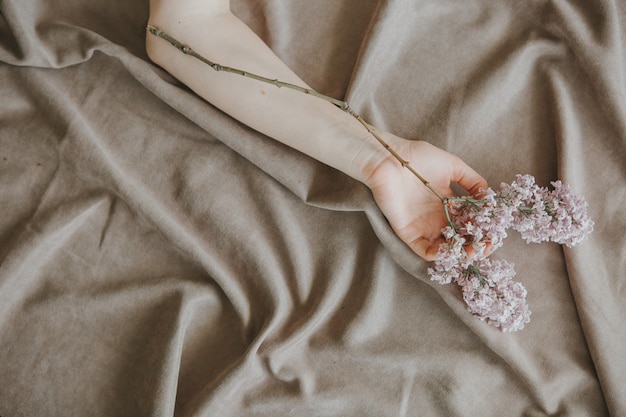 рука девушки с лиловой веткой на кровати на скомканном листе