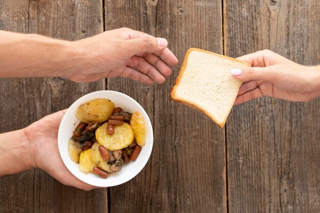 Hand giving bowl of food and bread to needy person