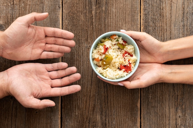 Free photo hand giving bowl of food to needy person