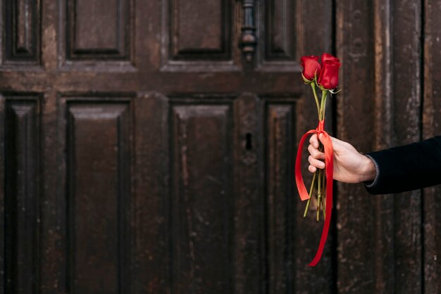 コピースペースで彼のカップルに赤いバラの花束を与える手