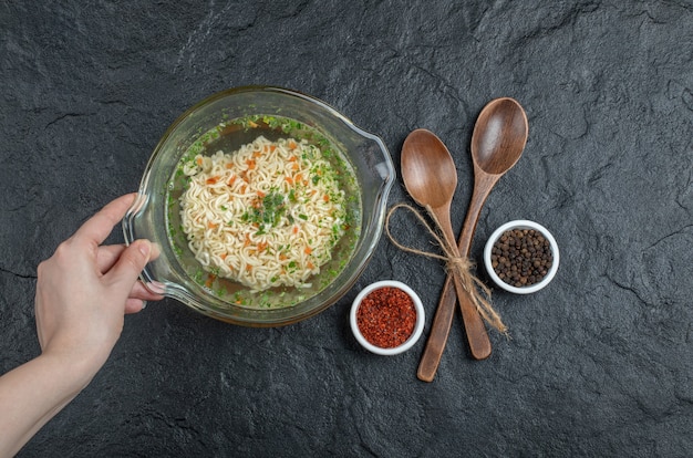 무료 사진 어두운 표면에 맛있는 국수와 함께 유리 접시를 들고 손.