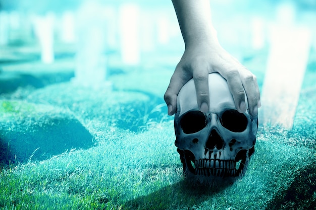 夜​の​シーン​の​背景​を​持つ​墓地​で​人間​の​頭蓋骨​を​持っている​手