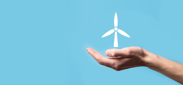 파란색 배경에 환경 에너지를 생산하는 풍차 아이콘을 손에 들고 있습니다. 프리미엄 사진