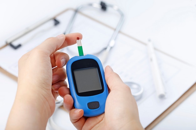 Free photo hand holding a blood glucose meter measuring blood sugar, the background is a stethoscope and chart file