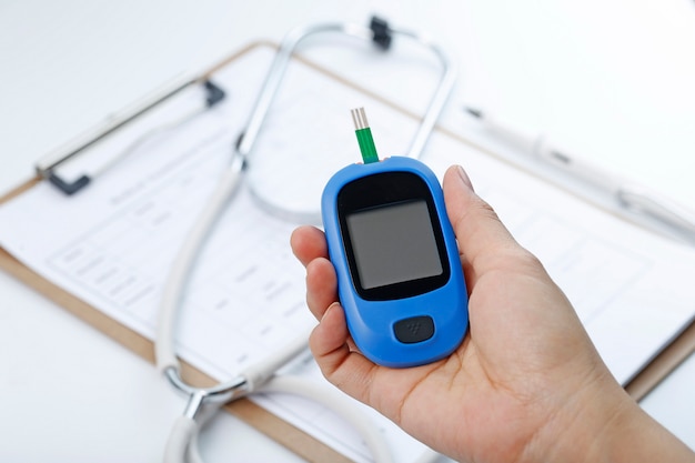 Free photo hand holding a blood glucose meter measuring blood sugar, the background is a stethoscope and chart file