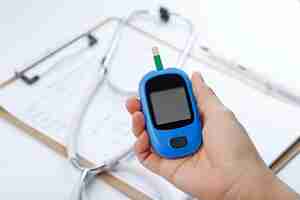 Free photo hand holding a blood glucose meter measuring blood sugar, the background is a stethoscope and chart file