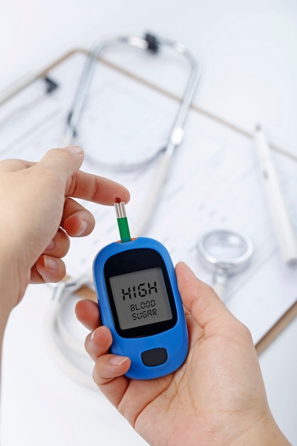 Free photo hand holding a blood glucose meter measuring blood sugar, the background is a stethoscope and chart file