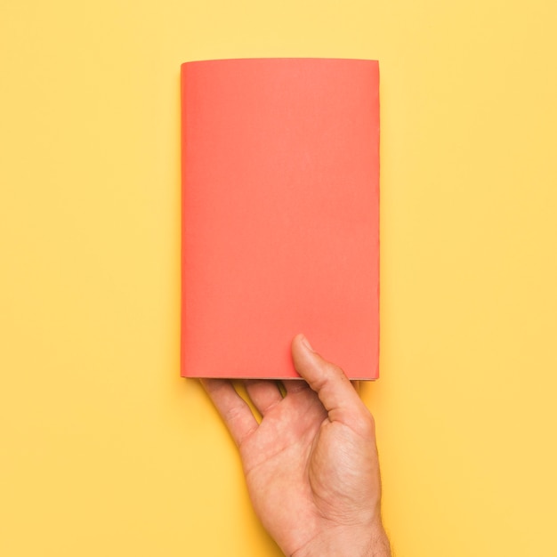 Hand holding book with red cover