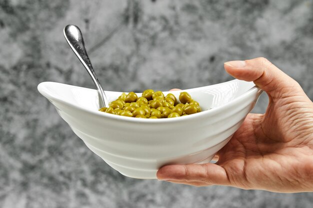 Hand holding a bowl of boiled green peas.