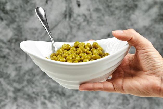 Hand holding a bowl of boiled green peas.