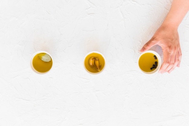 Hand holding bowl of oil on white textured backdrop