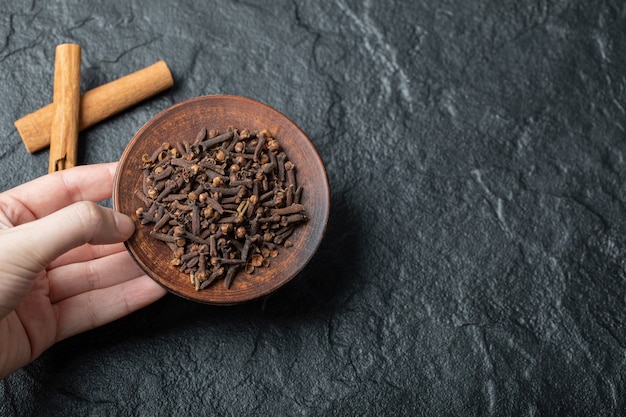 Hand holding a brown plate with dried clove. 