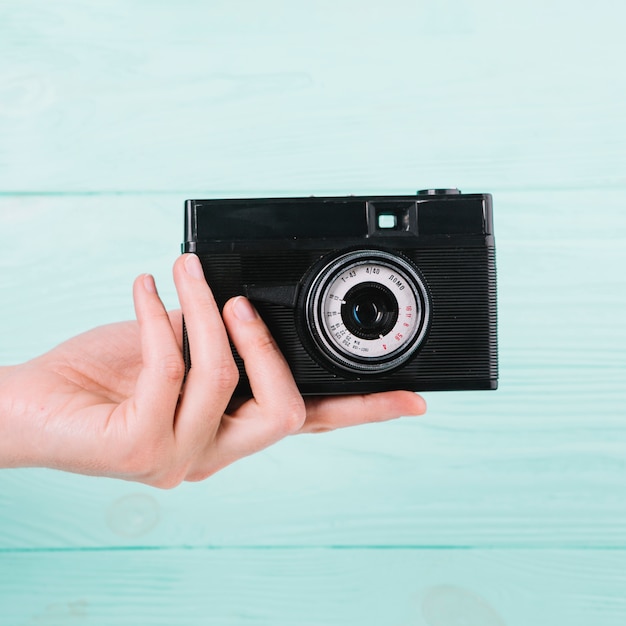 Free photo hand holding camera in front of blue background