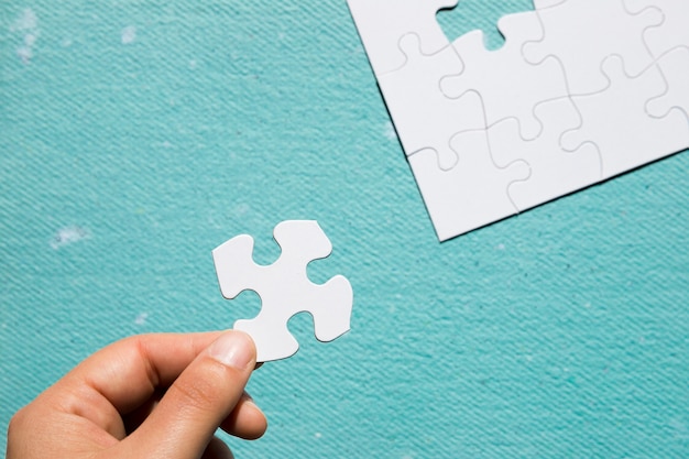 Hand holding cardboard white jigsaw puzzle over blue textured backdrop