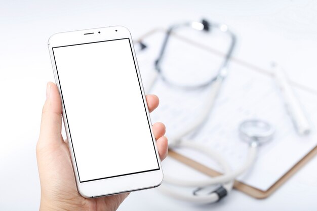 hand holding a cell phone in front of chart file and stethoscope