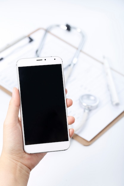 hand holding a cell phone in front of chart file and stethoscope