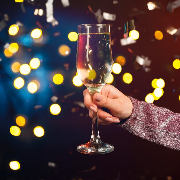 Hand holding champagne glass with confetti and bokeh effect