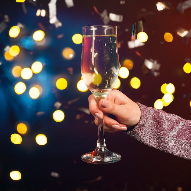 Hand holding champagne glass with confetti and bokeh effect