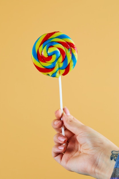 Hand holding colorful lollipop on orange wall.