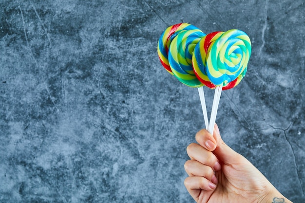 Free photo hand holding colorful lollipops on marble background.