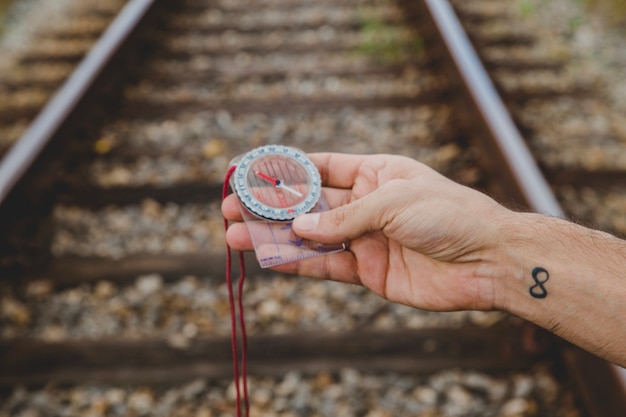 Free photo hand holding compass on train tracks