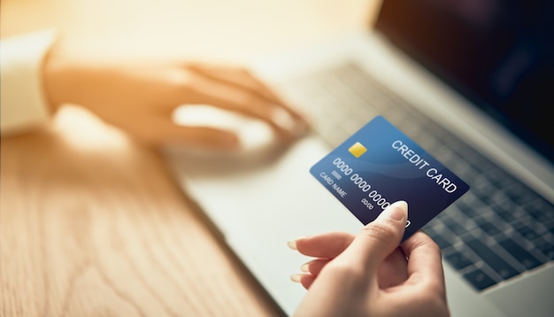 Рука, держащая кредитную карту и нажимающая на ноутбуке, вводит код оплаты за товар.