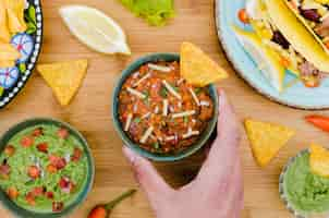 Free photo hand holding cup of garnish with nacho near mexican food