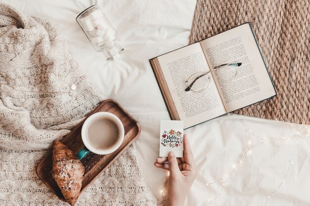 Hand holding cutaway near book, eyeglasses, food and plaid