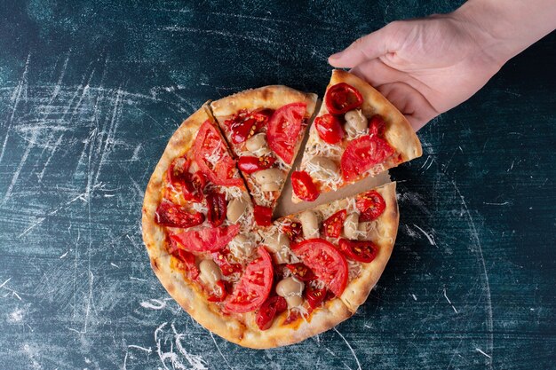 Hand holding delicious chicken pizza with tomatoes on marble.