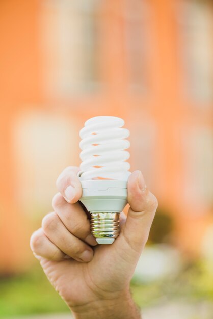 Hand holding energy saving compact fluorescent light bulb at outdoors