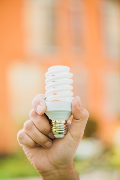 Hand holding energy saving compact fluorescent light bulb at outdoors