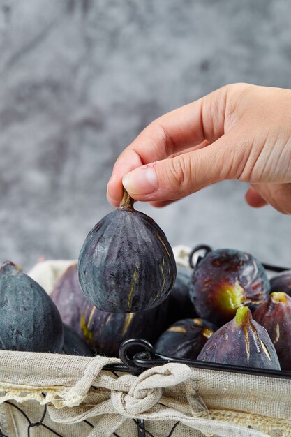 Hand holding a fig from the basket on marble.