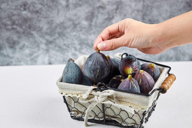 Hand holding a fig from the basket on white and marble.