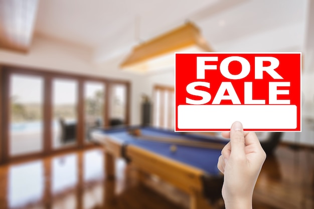 Рука на продажу дом знак с фоном интерьера дома