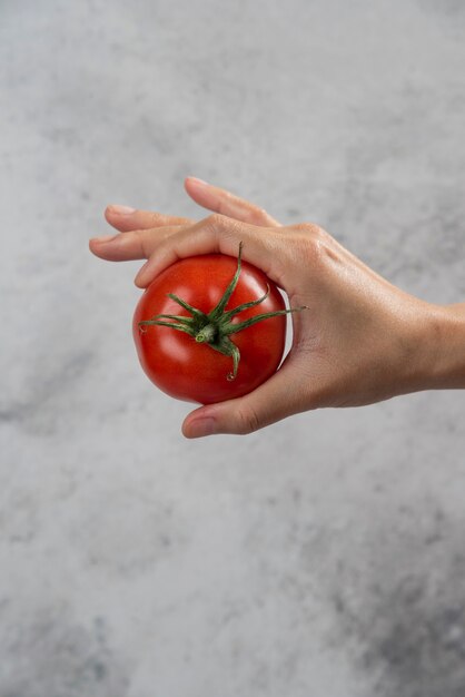 Hand holding a fresh red tomato on a marble background.